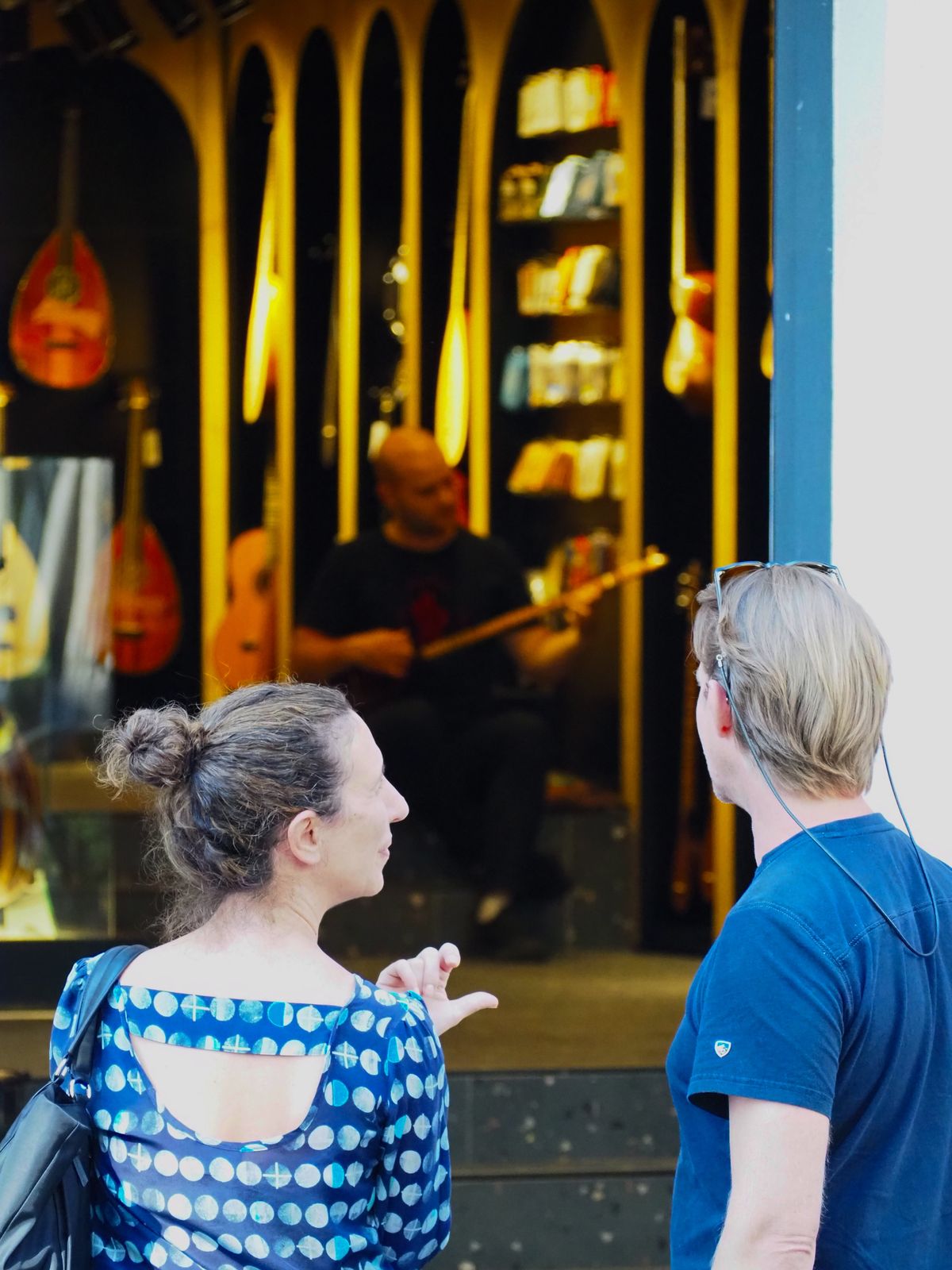 Two people looking into a warmly lit music shop where a musician is playing