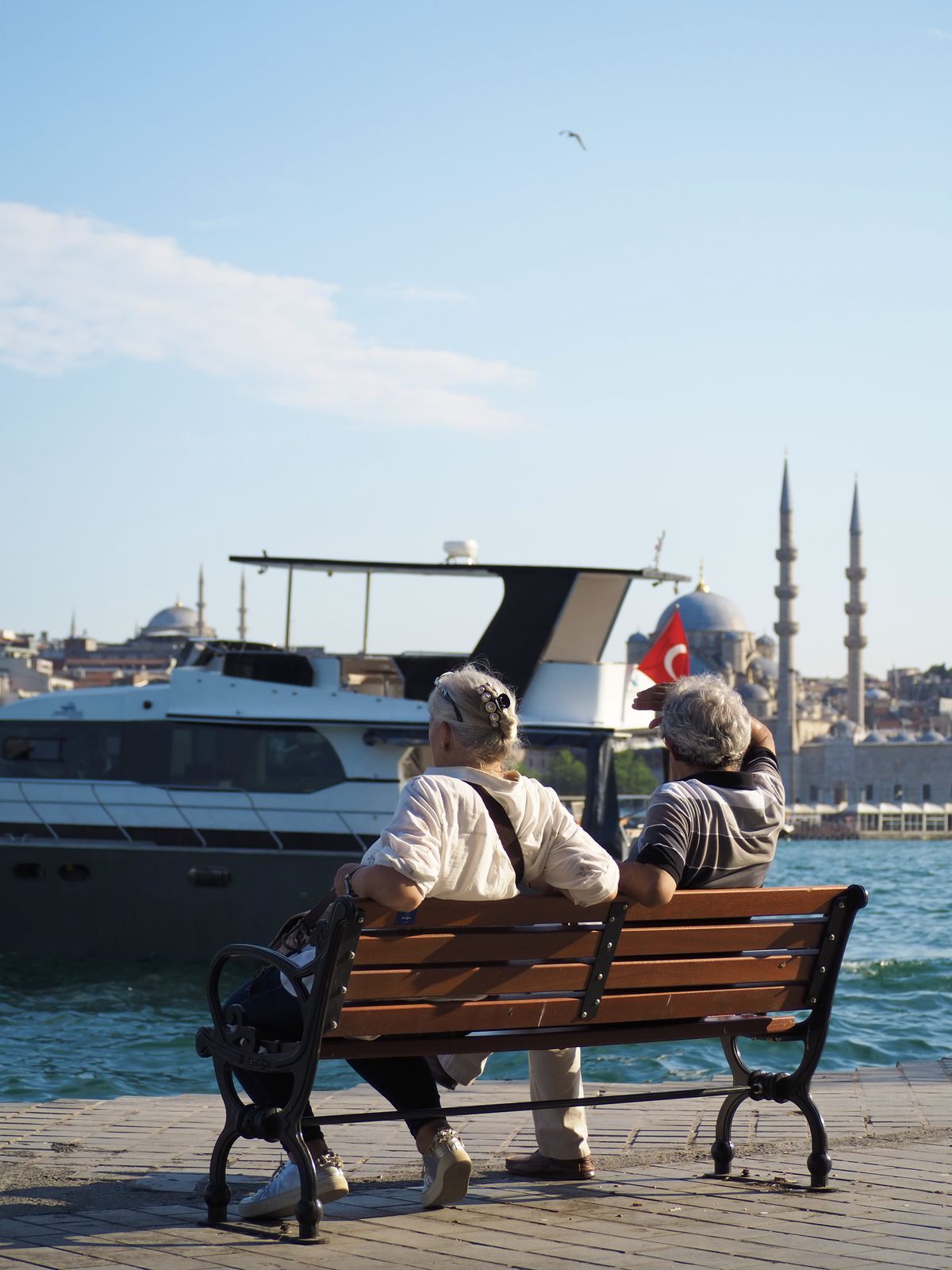 An elderly couple on a bench overlooking the water and a mosque skyline