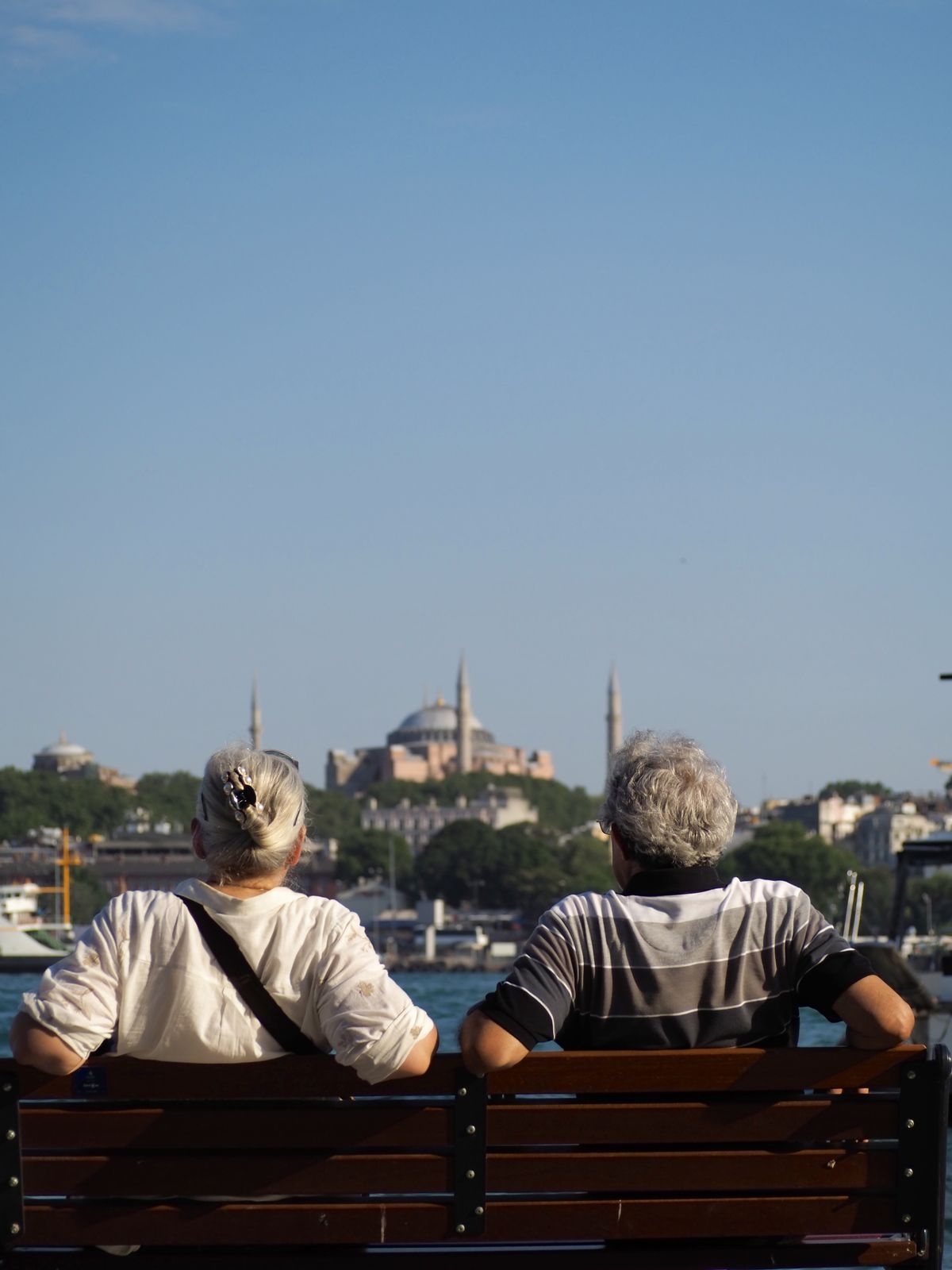 An elderly couple on a bench looking across the water toward Hagia Sophia